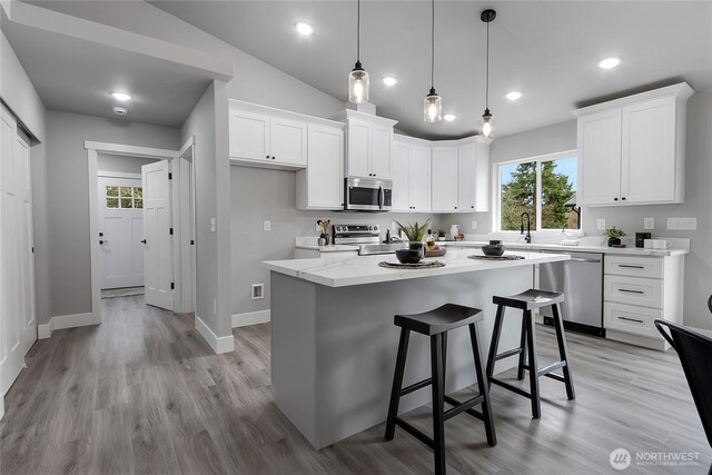 kitchen with light wood finished floors, a kitchen island, a breakfast bar area, appliances with stainless steel finishes, and white cabinetry