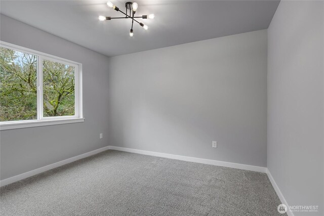 unfurnished room with a notable chandelier, carpet, and baseboards