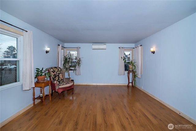 sitting room with an AC wall unit, baseboards, and wood finished floors