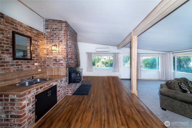 unfurnished living room with a wall mounted AC, lofted ceiling with beams, a healthy amount of sunlight, and a sink