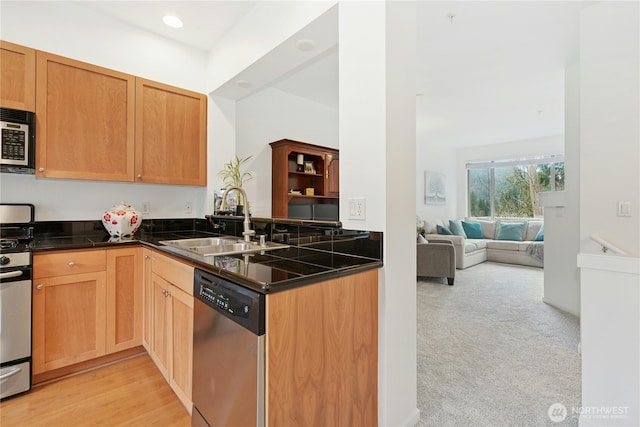 kitchen with a sink, light carpet, dark countertops, and appliances with stainless steel finishes