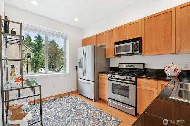 kitchen featuring recessed lighting, a sink, stainless steel appliances, light wood-style floors, and dark countertops