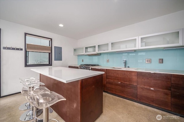 kitchen featuring a kitchen island, glass insert cabinets, stainless steel range with gas stovetop, light countertops, and a sink