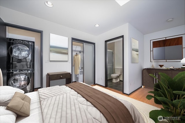 bedroom with wood finished floors, recessed lighting, connected bathroom, stacked washer / dryer, and baseboards