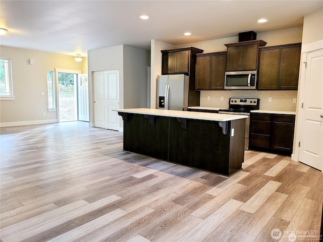 kitchen with a kitchen bar, a center island, light wood-style floors, appliances with stainless steel finishes, and light countertops