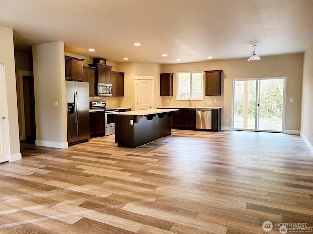 kitchen featuring dark brown cabinets, a center island, light wood-type flooring, light countertops, and appliances with stainless steel finishes