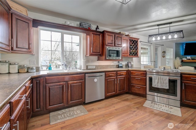 kitchen with decorative light fixtures, light wood-type flooring, appliances with stainless steel finishes, a peninsula, and a sink