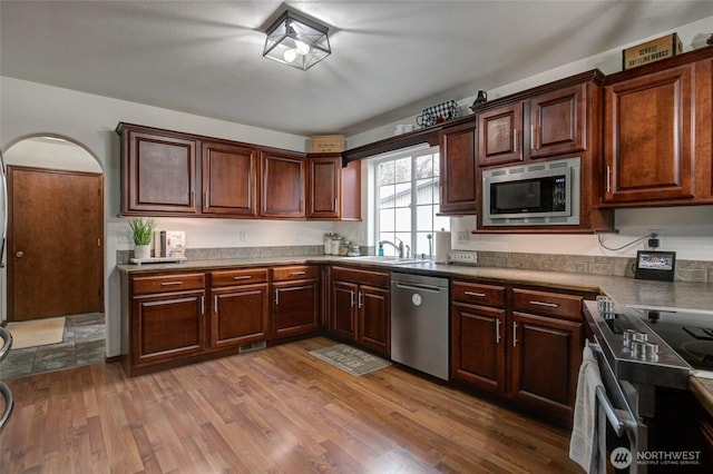 kitchen featuring visible vents, dark brown cabinets, light wood-type flooring, appliances with stainless steel finishes, and a sink