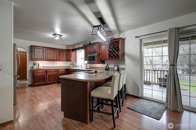 kitchen featuring stainless steel microwave, a kitchen bar, light wood-type flooring, a peninsula, and a sink