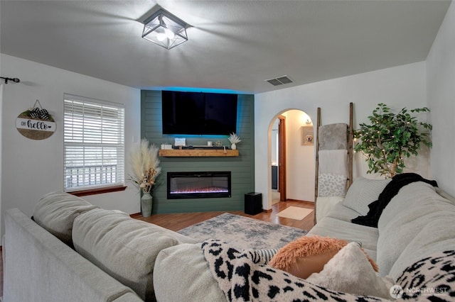 living room featuring wood finished floors, arched walkways, visible vents, and a large fireplace