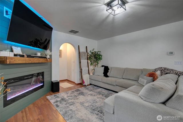 living area featuring wood finished floors, visible vents, arched walkways, and a glass covered fireplace