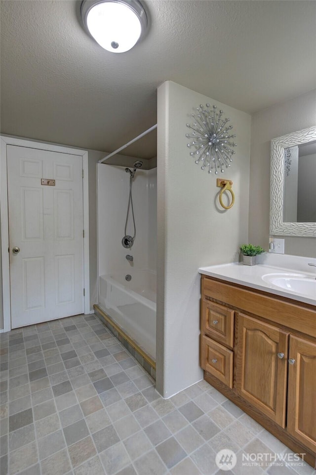 bathroom with a textured ceiling, vanity, and  shower combination