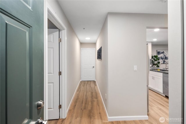 hallway featuring light wood-style flooring, baseboards, and a sink