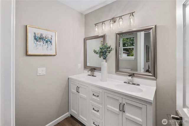 full bathroom featuring double vanity, wood finished floors, baseboards, and a sink