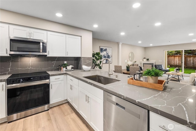 kitchen with dark stone counters, a sink, white cabinets, light wood-style floors, and appliances with stainless steel finishes