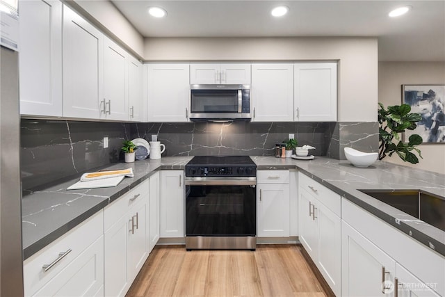 kitchen with stainless steel microwave, light wood-style flooring, range with electric stovetop, and white cabinets