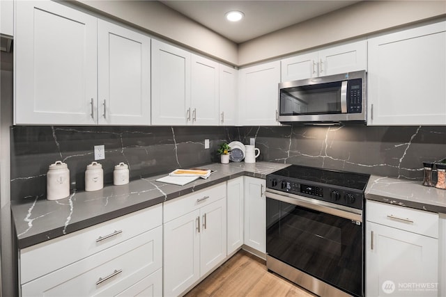 kitchen with light wood finished floors, electric range, white cabinets, stainless steel microwave, and backsplash