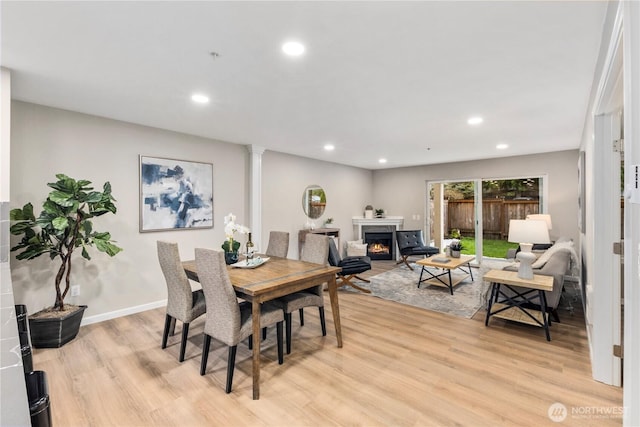 dining space with decorative columns, recessed lighting, light wood-type flooring, and a lit fireplace