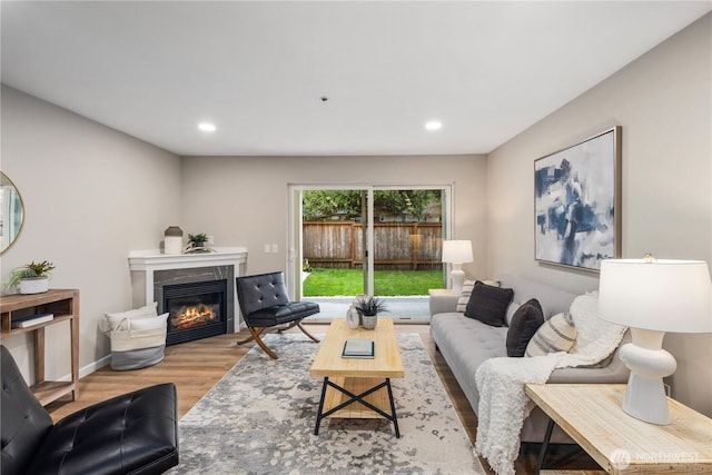 living room featuring a glass covered fireplace, recessed lighting, baseboards, and wood finished floors