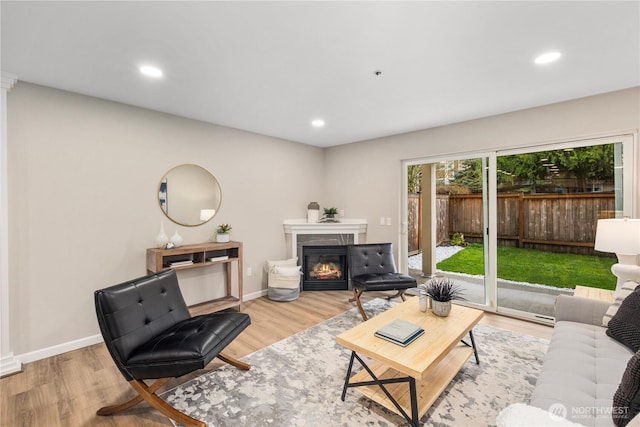 living area with a glass covered fireplace, recessed lighting, wood finished floors, and baseboards