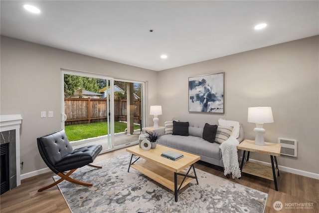 living area with recessed lighting, wood finished floors, baseboards, and a premium fireplace