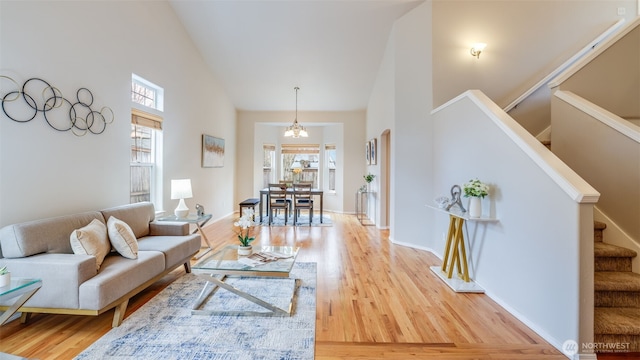 living room featuring high vaulted ceiling, stairs, light wood-type flooring, and baseboards