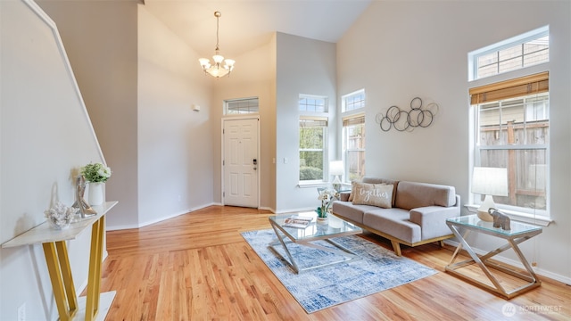 living room featuring baseboards, a notable chandelier, a towering ceiling, and light wood finished floors