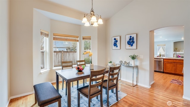 dining area featuring a chandelier, arched walkways, baseboards, and light wood-style floors