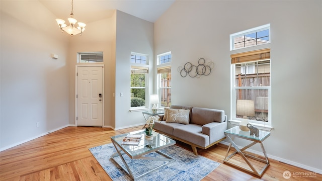 living area featuring a notable chandelier, wood finished floors, baseboards, and high vaulted ceiling