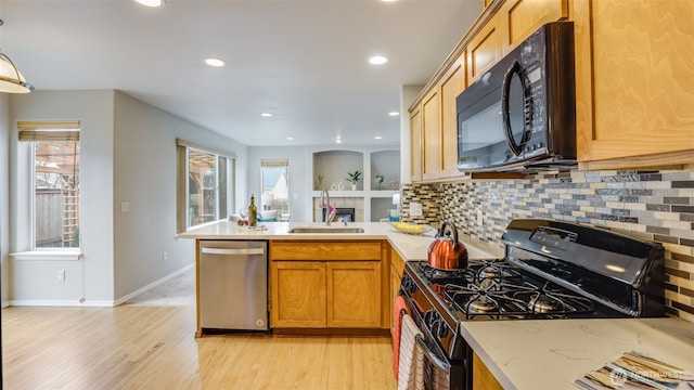 kitchen with a sink, stainless steel appliances, a peninsula, and light wood finished floors