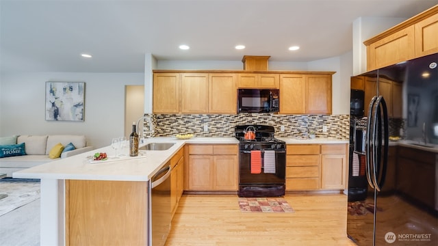 kitchen with black appliances, a peninsula, tasteful backsplash, and a sink