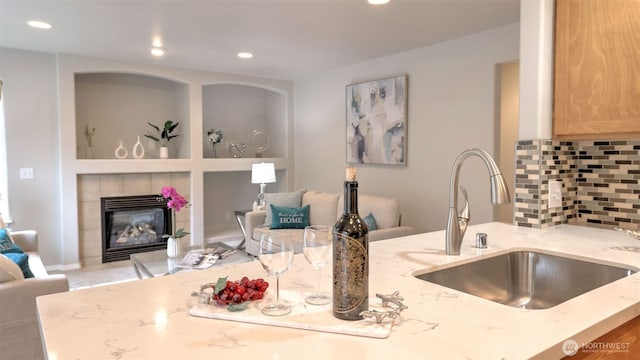 kitchen with backsplash, open floor plan, light stone counters, a tile fireplace, and a sink