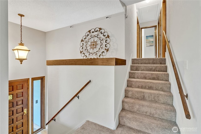 staircase with a textured ceiling, attic access, and carpet flooring