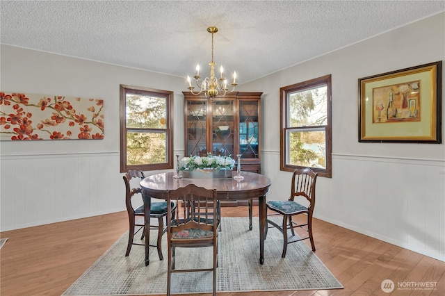 dining space with a wainscoted wall, a textured ceiling, an inviting chandelier, and wood finished floors