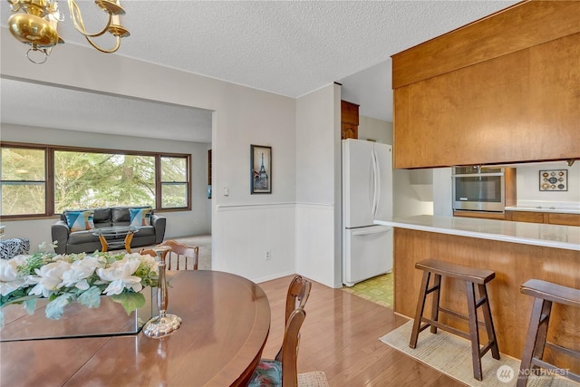 dining space with a notable chandelier, a textured ceiling, and light wood-style floors