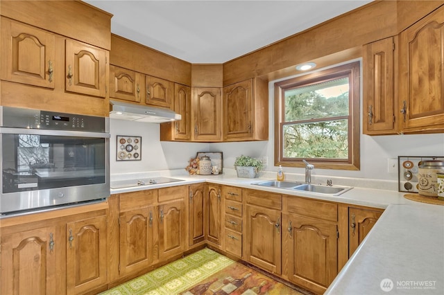 kitchen with oven, black electric stovetop, under cabinet range hood, brown cabinets, and a sink