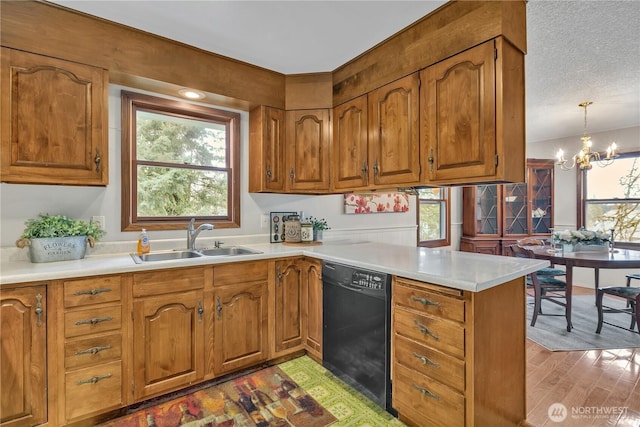 kitchen featuring brown cabinetry, a peninsula, a sink, black dishwasher, and a chandelier