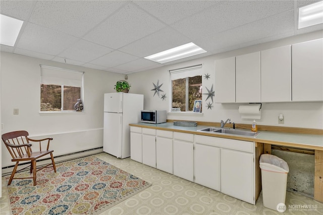 kitchen with stainless steel microwave, baseboard heating, freestanding refrigerator, a paneled ceiling, and a sink