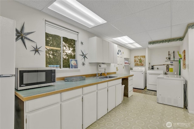 kitchen with washer and clothes dryer, stainless steel microwave, water heater, freestanding refrigerator, and a paneled ceiling