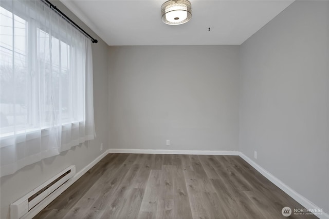 empty room featuring wood finished floors, baseboards, and a baseboard radiator