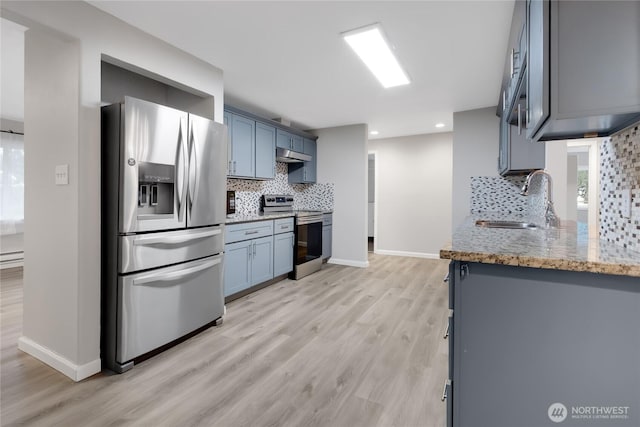 kitchen featuring a sink, light stone counters, under cabinet range hood, appliances with stainless steel finishes, and light wood finished floors