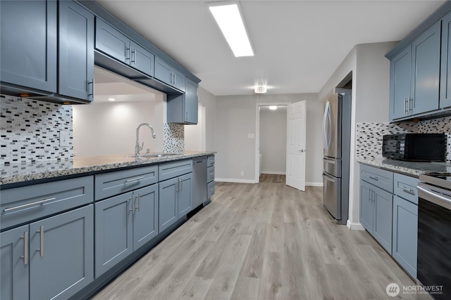 kitchen with blue cabinetry, light stone countertops, appliances with stainless steel finishes, light wood-style floors, and a sink