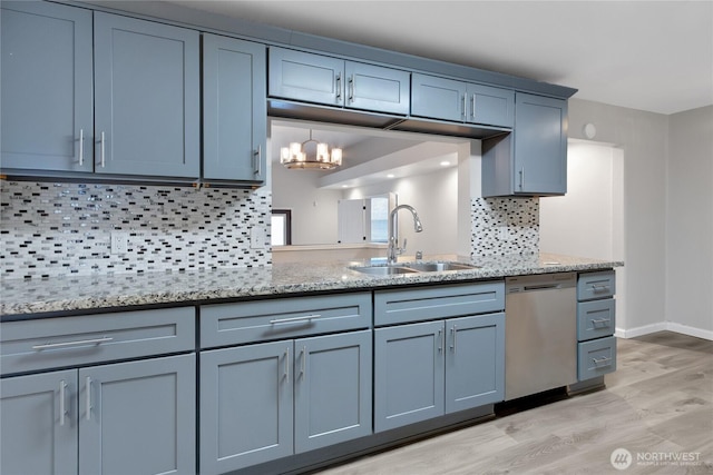 kitchen with light stone countertops, light wood-style flooring, a sink, decorative backsplash, and stainless steel dishwasher