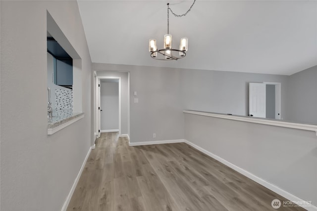 unfurnished dining area featuring a notable chandelier, baseboards, and wood finished floors