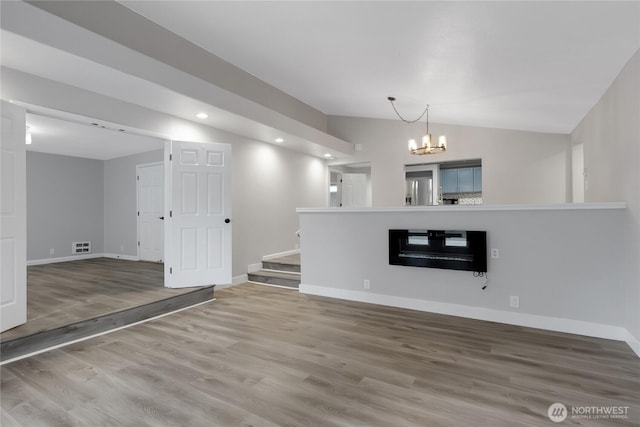 unfurnished living room with a notable chandelier, wood finished floors, recessed lighting, baseboards, and vaulted ceiling