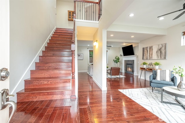 stairway featuring a glass covered fireplace, baseboards, wood finished floors, and a ceiling fan