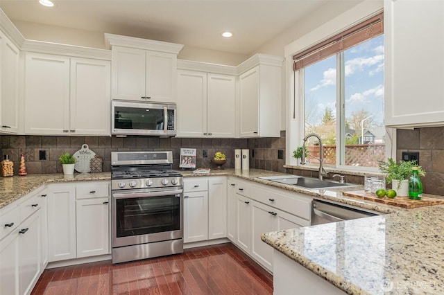 kitchen with a sink, backsplash, dark wood-style floors, appliances with stainless steel finishes, and white cabinets