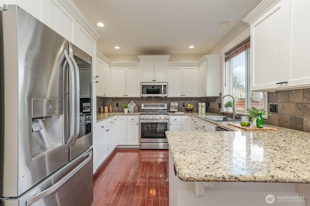 kitchen with a peninsula, a sink, stainless steel appliances, dark wood-type flooring, and white cabinetry