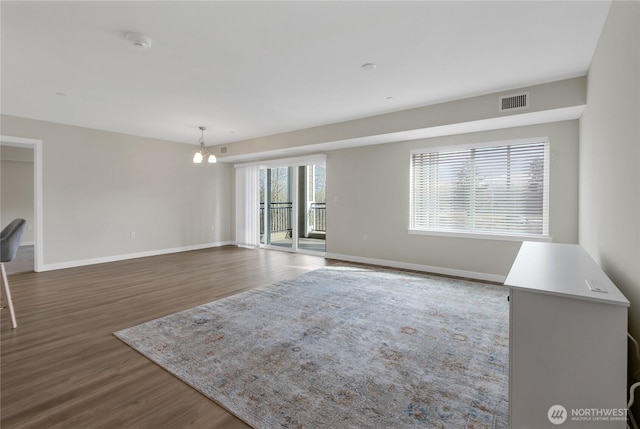 unfurnished living room with visible vents, baseboards, an inviting chandelier, and dark wood finished floors