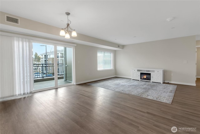 unfurnished living room with a chandelier, visible vents, baseboards, and wood finished floors